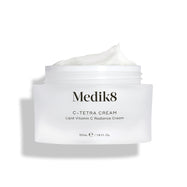 Barattolo aperto di crema Medik8 C-Tetra, mostrato su uno sfondo bianco pulito con ombre morbide. Il barattolo in vetro satinato bianco presenta il logo Medik8 ed è etichettato come C-TETRA CREAM Lipid Vitamin C Radiance Cream da 50 mL. Una spessa spirale di crema bianca è visibile sulla parte superiore del barattolo, evidenziandone la consistenza idratante.