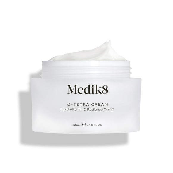 Barattolo aperto di crema Medik8 C-Tetra, mostrato su uno sfondo bianco pulito con ombre morbide. Il barattolo in vetro satinato bianco presenta il logo Medik8 ed è etichettato come C-TETRA CREAM Lipid Vitamin C Radiance Cream da 50 mL. Una spessa spirale di crema bianca è visibile sulla parte superiore del barattolo, evidenziandone la consistenza idratante.-9