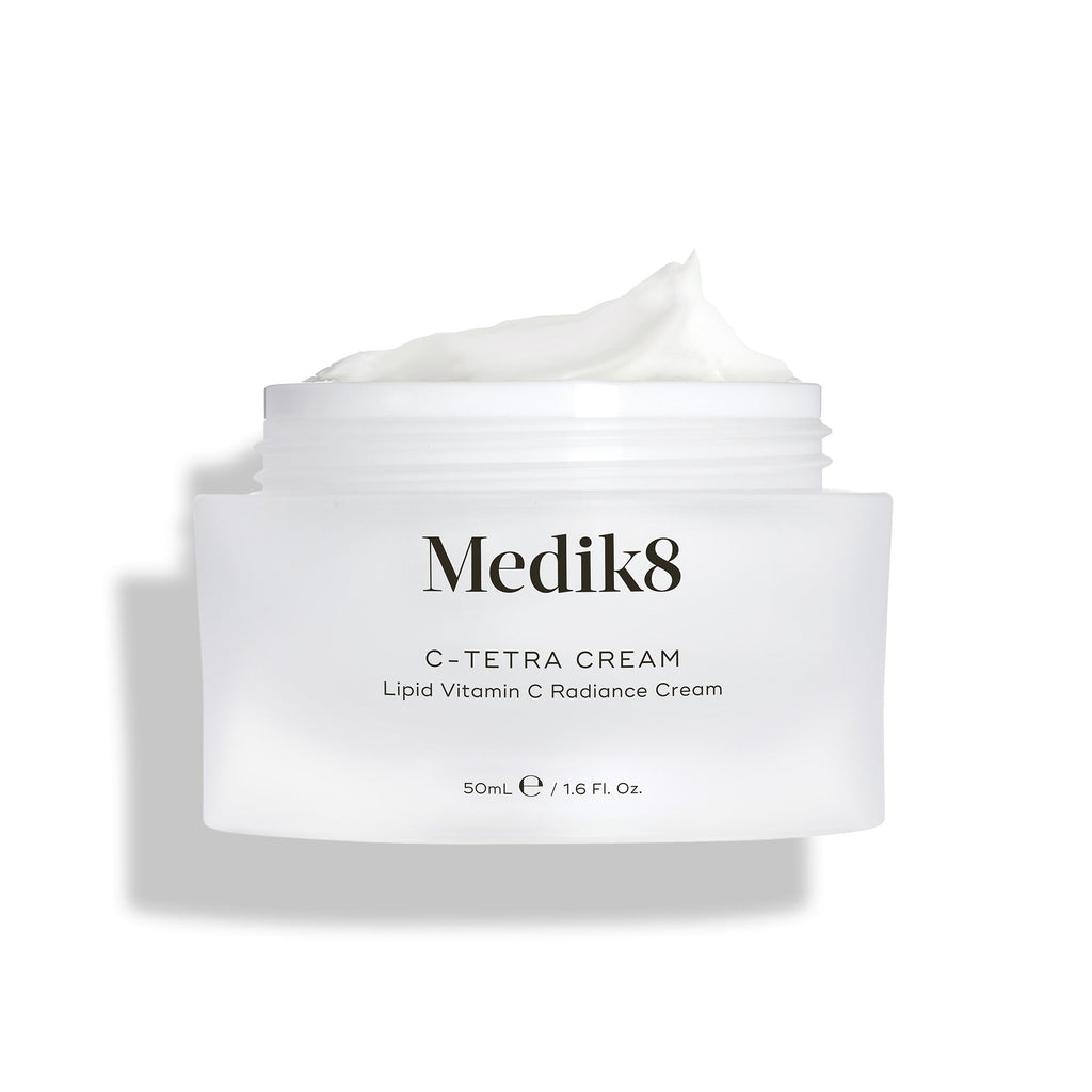 Barattolo aperto di crema Medik8 C-Tetra, mostrato su uno sfondo bianco pulito con ombre morbide. Il barattolo in vetro satinato bianco presenta il logo Medik8 ed è etichettato come C-TETRA CREAM Lipid Vitamin C Radiance Cream da 50 mL. Una spessa spirale di crema bianca è visibile sulla parte superiore del barattolo, evidenziandone la consistenza idratante.