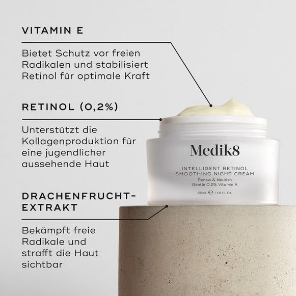 Nahaufnahme der Intelligent Retinol Smoothing Night Cream. Zu sehen ist ein weißer Tiegel mit Creme und Etiketten mit Hinweisen auf die Inhaltsstoffe. Der Hintergrund ist hell und strukturiert. Textfelder heben Vitamin E, Retinol (0,2 %) und Drachenfruchtextrakt hervor.-hover-1