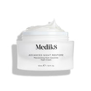 Il barattolo di Medik8 Advanced Night Restore è mostrato aperto con una ricca punta di crema bianca sulla superficie, su uno sfondo bianco pulito che ne evidenzia la texture liscia e rigenerante. Il testo nero sul barattolo riporta Rejuvenating Multi-Ceramide Night Cream.