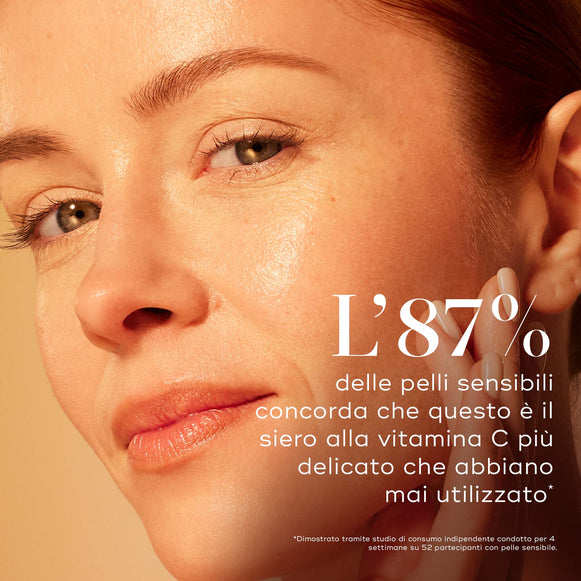 Primo piano di una modella con pelle luminosa che si tocca delicatamente la guancia su un caldo sfondo sfumato. Il testo in italiano evidenzia che l'87% delle pelli sensibili concorda che questo è il siero alla vitamina C più delicato che abbiano mai utilizzato, dimostrato tramite uno studio di consumo indipendente.-hover-6